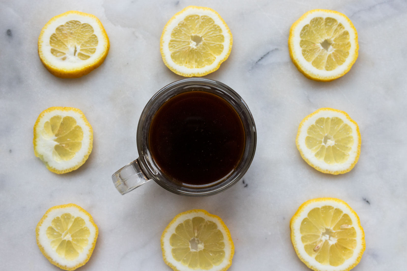 A cup of black coffee on a kitchen counter surrounded by fresh lemon slices, creating a bold and refreshing aesthetic.